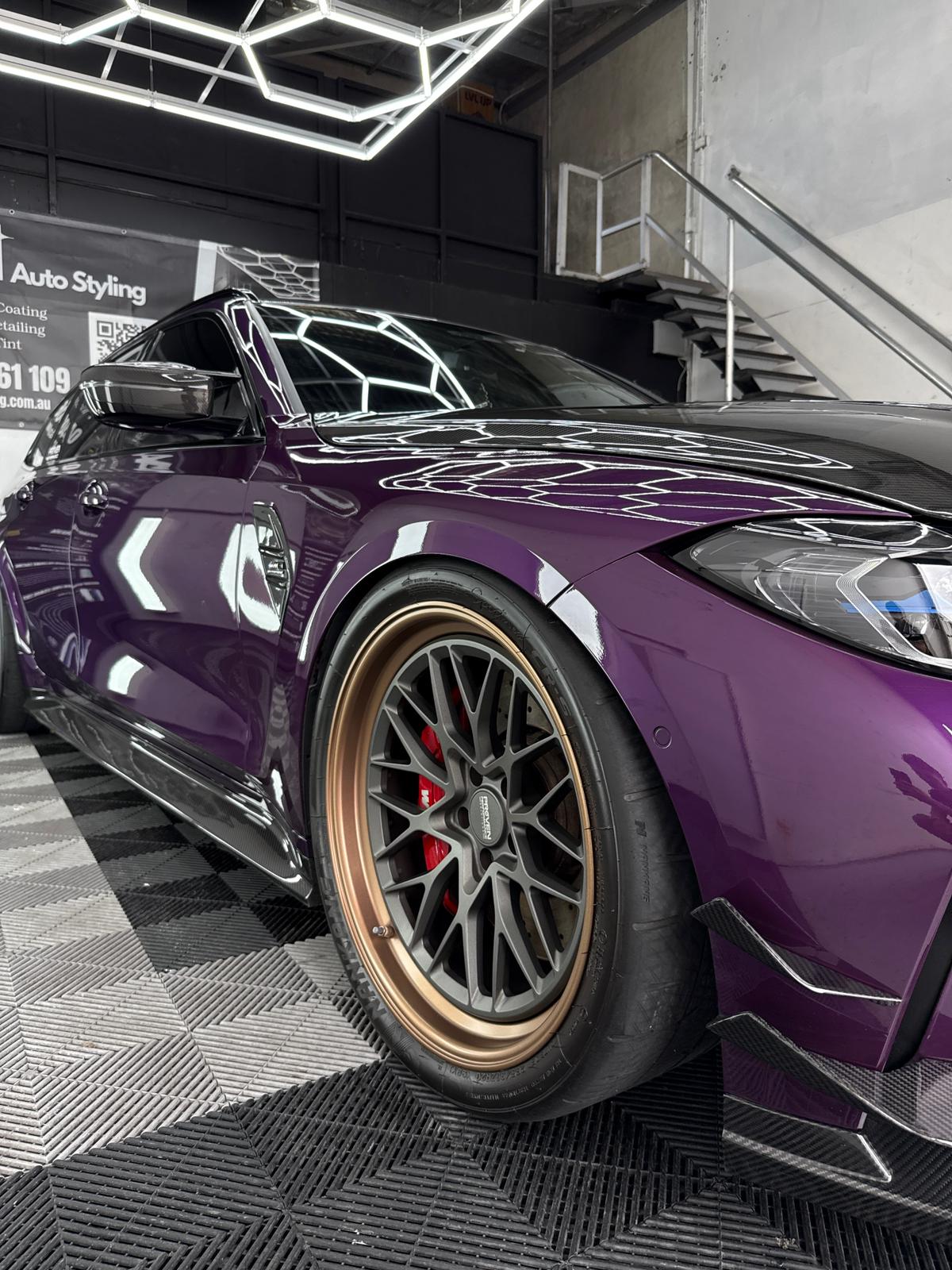 Purple BMW M3 with bronze BBS wheels close-up, ceramic coated paint reflecting the hexagonal LED ceiling