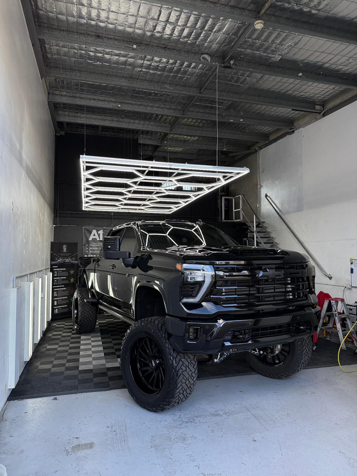 Black lifted Chevy Silverado HD2500 with tinted glass in the A1 Auto Styling workshop, hexagonal LED ceiling above